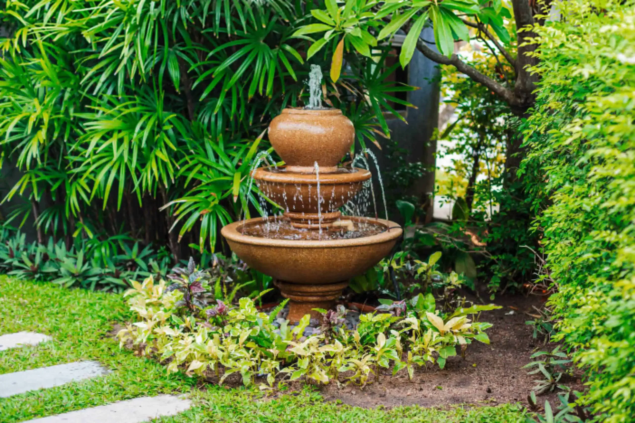 A three-tiered clay water feature surrounded by green plants and shrubs is situated in a lush garden maintained meticulously by HOA services.