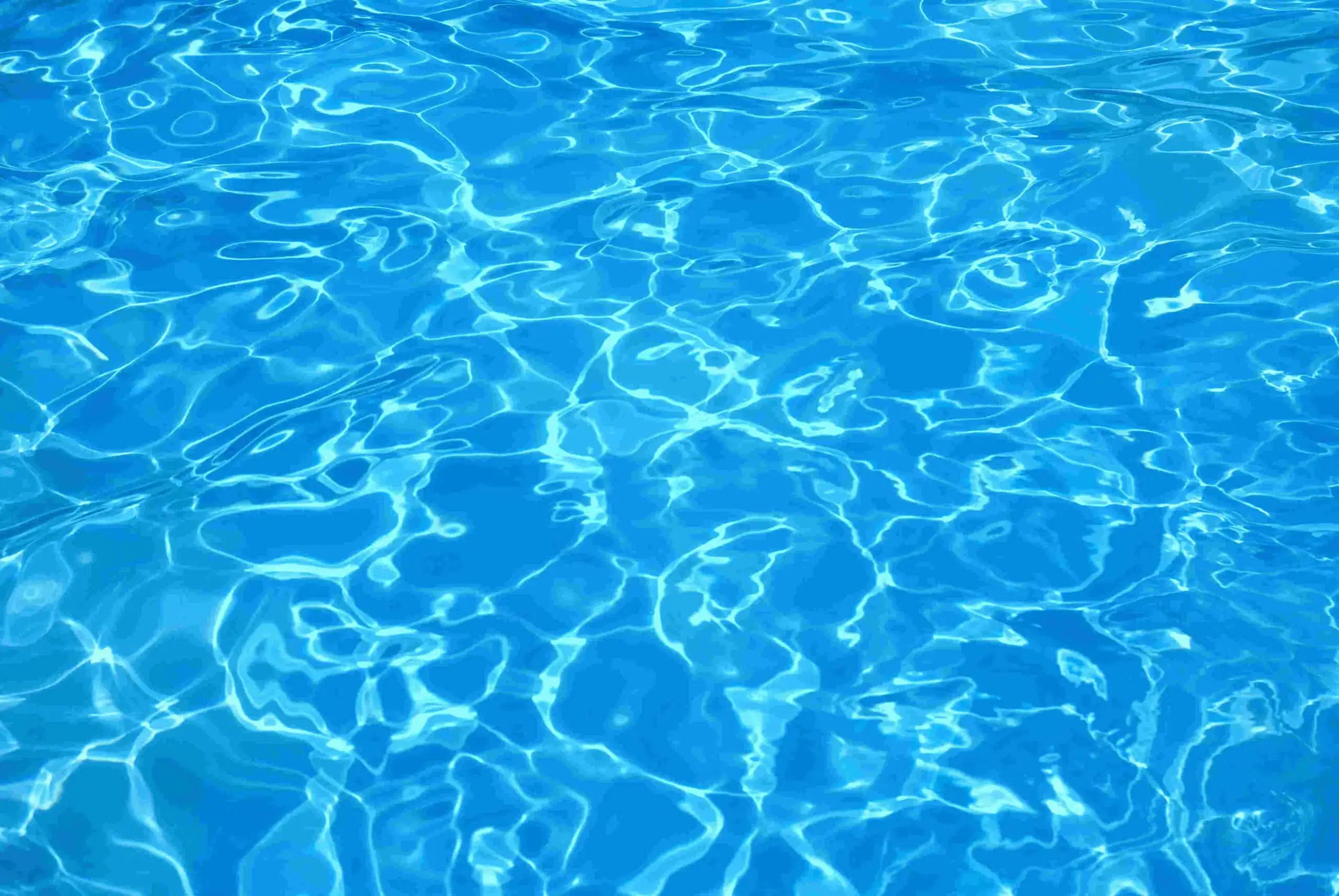 A clear, sunlit swimming pool surface with shimmering blue water and light reflections creating a wavy pattern, maintained to perfection by professional Commercial Pool Services.