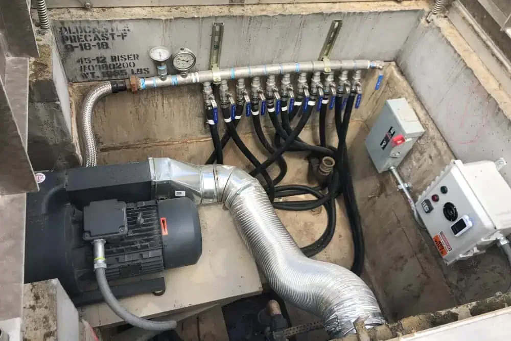 A mechanical pond pump and filtration system with multiple pipes, pressure gauges, and control panels installed in a concrete pit. Black hoses and metallic ducts are connected to an electric motor with a ventilation system, providing crucial support services for the business center's operations.