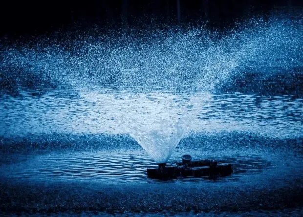 A blue fountain spraying water in a pond with an aerator.