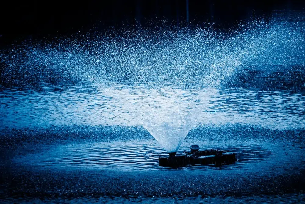 A blue fountain aerating water in a pond.