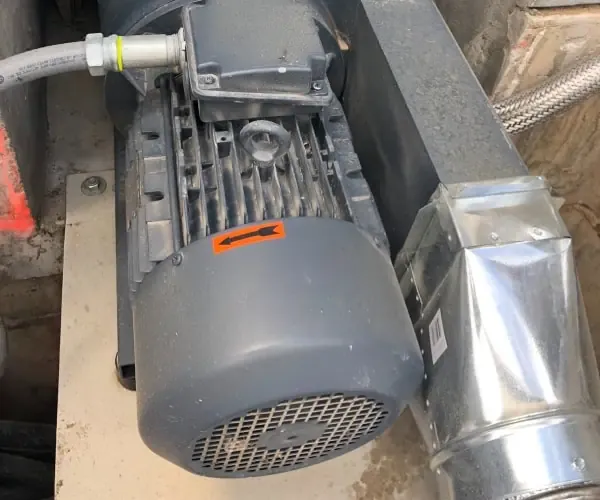 A pond pool pump motor is resting atop a pipe in a building, possibly in need of Aquatic Equipment Services.