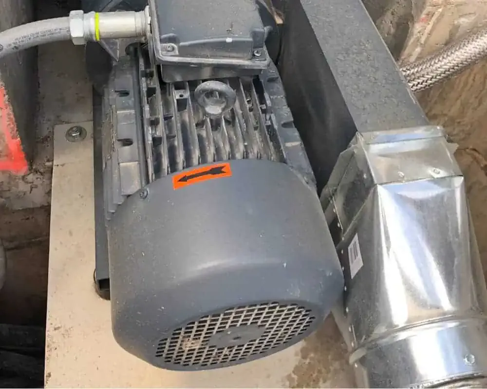 A motor is sitting on top of a pipe in a basement.