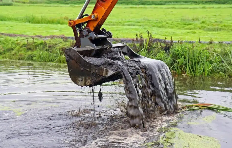 An excavator is pouring water into a pond, providing water feature services for a golf course.