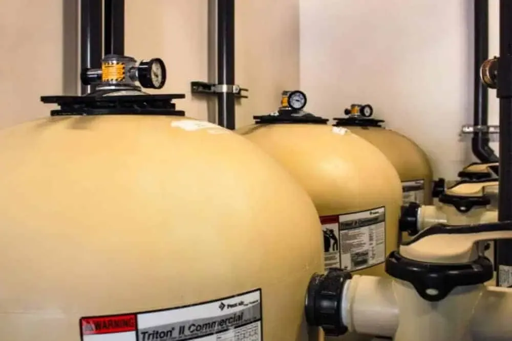 Large beige commercial water filtration tanks in a row, equipped with pressure gauges and warning labels, are essential to the business center's services.