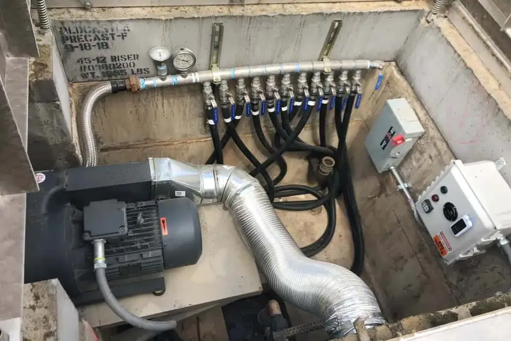 A mechanical pond pump and filtration system with multiple pipes, pressure gauges, and control panels installed in a concrete pit. Black hoses and metallic ducts are connected to an electric motor with a ventilation system, providing crucial support services for the business center's operations.