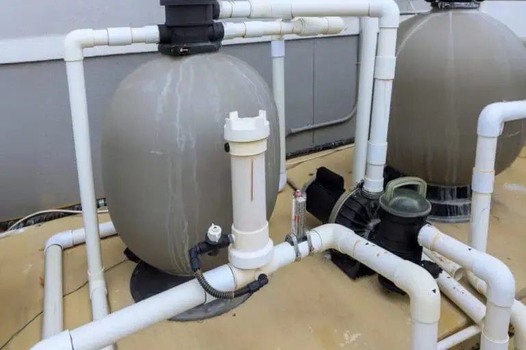 A pool filtration system with connected pipes and tanks is shown, essential for lake maintenance. The equipment is placed against a wall on a concrete surface.