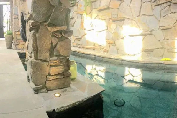 A pool with a stone wall, a water feature, and pillars.